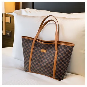 Detail of a large brown checkered tote bag with gold logo on a white bed