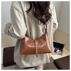 Detailed view of a caramel brown leather underarm bag featuring decorative metal rivet belts