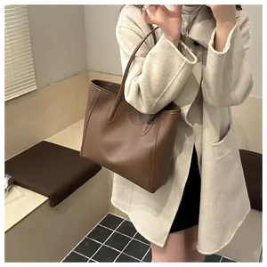 Detail of a large brown leather tote bag held by a model in a minimalist winter setting