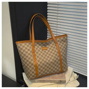 Detail of printed tote bag with brown leather handles and gold nameplate in natural light