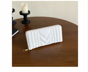 Close-up of a white quilted long wallet for women with V-stitch pattern on a dark wood table