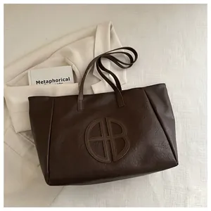 Detail of deep brown leather tote bag with circular AB logo on a soft blazer