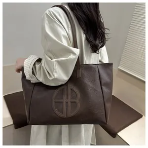 Detailed view of dark brown faux leather tote bag with embossed logo and long shoulder strap