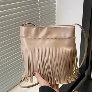 Beige PU leather crossbody bag with long fringes and thin shoulder strap in hand
