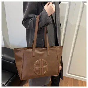 Close-up of a brown tote bag with circular logo detail worn with a dark grey wool coat