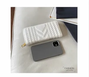 White quilted long wallet with V-stitch texture shown beside a phone for scale