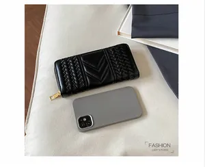 Detail of black long wallet with V-quilting and gold zipper next to a smartphone