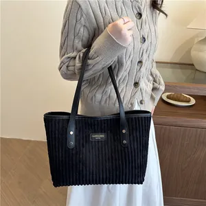 Black corduroy tote bag with leather handles shown in a stylish indoor lifestyle setting