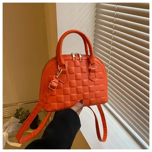 Detailed macro shot of bright orange quilted checkered shell bag with golden zipper hardware