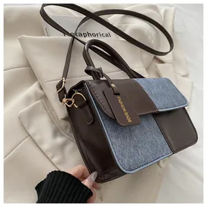 Detail of trendy color-block handbag showing brown leather and blue denim stitching