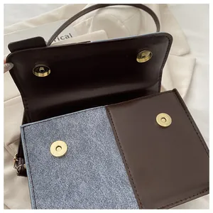 Detail of blue denim and brown leather contrast flap with dual golden magnetic buckles
