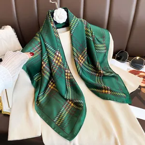Dark green plaid silk scarf with geometric patterns displayed on a beige sweater