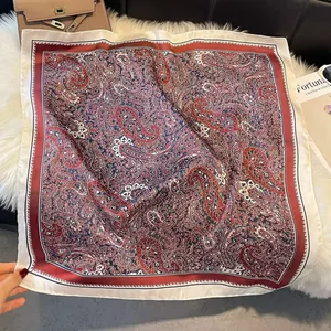 Flat lay of an elegant paisley silk scarf with warm red and cream tones on soft plush fabric