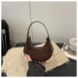 Detail of a minimalist dark brown suede crescent bag with a gold zipper and slim handle