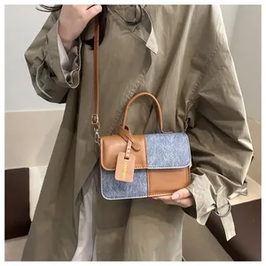 Detail of a brown leather and blue fabric patchwork handbag worn with a khaki trench coat