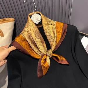 Detailed view of silk square scarf featuring gold and brown paisley patterns with a smooth texture