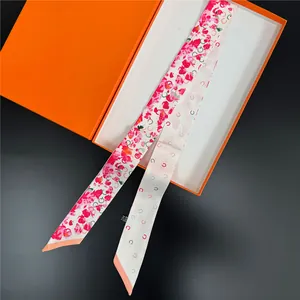 Détail d'un foulard twilly floral dans sa boîte orange avec gros plan sur la texture