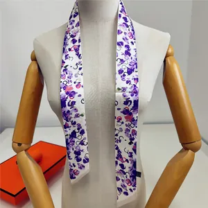 Détail d'un foulard twilly violet à fleurs noué sur un mannequin près d'une boîte