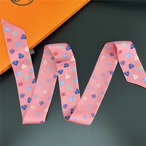Makro-Detail eines rosa Seidenschals mit Herzmuster und oranger Geschenkbox