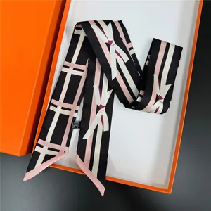 Pink and black ribbon scarf with bow patterns in an orange luxury gift box on a table