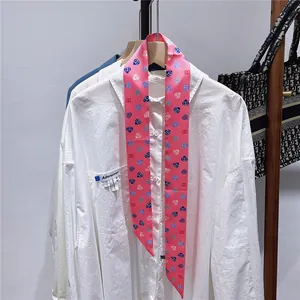 Detailansicht eines langen rosa Seidenschals mit Herzmuster an einem weißen Hemdkragen
