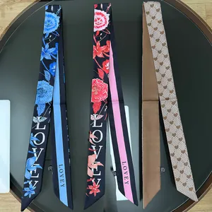 Tre foulard lunghi e stretti in seta con motivi a cuori e fiori su un tavolo