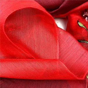 Dettaglio macro della sciarpa in seta rossa con ricami floreali e bordi rifiniti bene
