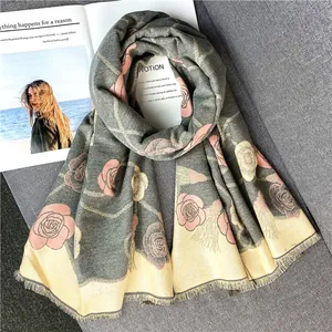 Détail d'une écharpe en imitation cachemire vert gris avec motifs roses et franges