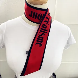 Detalle de un pañuelo de seda rojo estrecho con borde negro y estampado C'est le réalisme