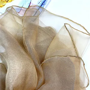 Dettaglio della sciarpa in seta e lana dorata con bordi decorati con strass scintillanti