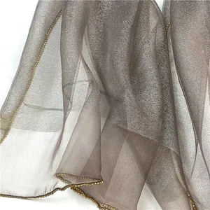 Dettaglio di sciarpa in seta e lana grigio scuro con glitter metallici e bordo dorato