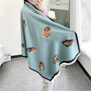 Close-up of light blue shawl featuring orange feather prints and beige fringe trim details