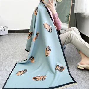 Detail showing elegant light blue scarf with orange feather prints and yellow fringe