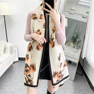Close-up of elegant beige cashmere-like shawl with orange tulip prints and black tassel edges