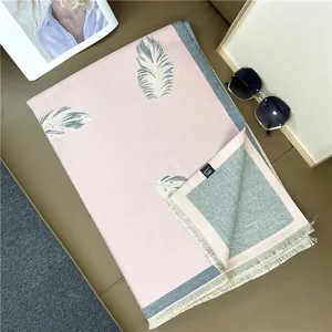 Detail of pink and gray scarf with artistic feather prints, fringes, and care label