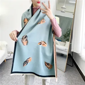 Light blue scarf with brown feather print and white fringes shown on a model