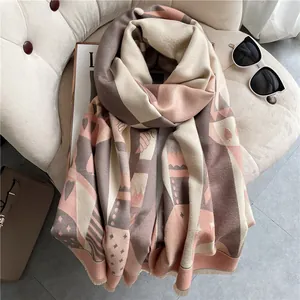 Thick warm winter scarf with pink geometric patterns and tassels on beige soft velvet chair