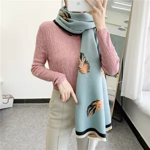 Light blue scarf with orange feather print and black trim worn over pink sweater