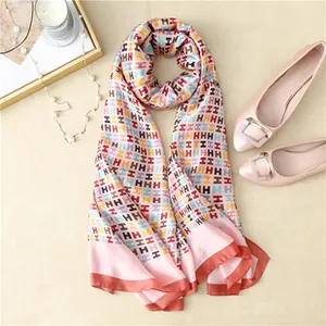 Detail view of pink silk scarf with H-pattern print and contrasting orange borders