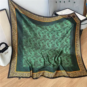 Detail of green floral silk scarf with golden leopard print border on a grey sofa