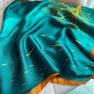 Detailed close-up of dark teal silk scarf with orange borders and golden tree patterns