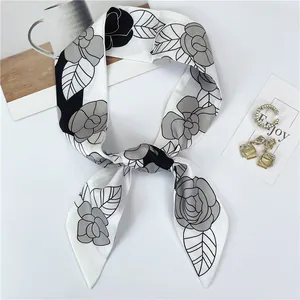 Detalle de un pañuelo de seda largo con estampado de camelia y joyas sobre mesa blanca