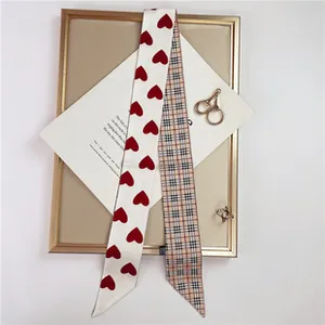 Close-up of dual-sided twilly scarf featuring red heart print and classic plaid pattern