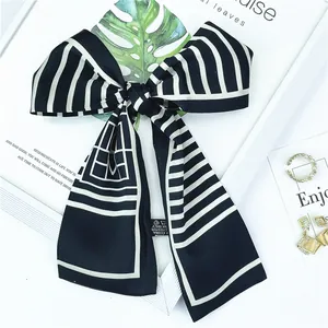 Détail d'un foulard en soie à rayures noires et blanches noué en nœud avec des perles