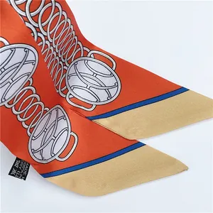 Close-up of orange silk twilly scarf with golden chain patterns and diagonal twill texture