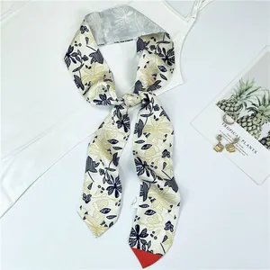 Détail d'un foulard en soie twilly crème à motif floral tropical noué sur un col blanc