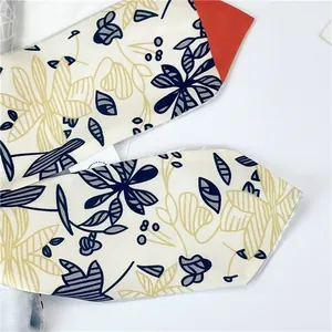 Détail macro d'un foulard twilly à fleurs avec pointes orange et imprimé botanique élégant