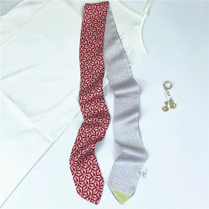 Detail of red geometric silk scarf twilly styled on white camisole with metal jewelry