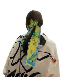 Lungo foulard di seta gialla con motivo astratto usato come elastico decorativo per capelli