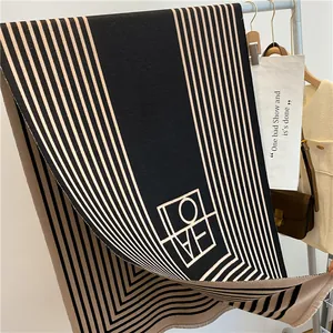 Vue détaillée de l'écharpe à rayures géométriques noir et beige avec logo et franges